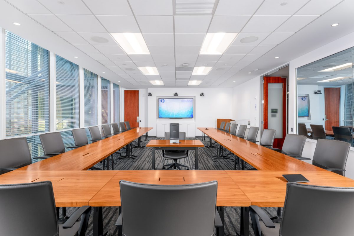Conference Room 18 at JAMS NY IAC — reverse corner view, cherry horseshoe to JAMS display + twin PTZ cams, louvered windows, adjacent boardroom through glass.