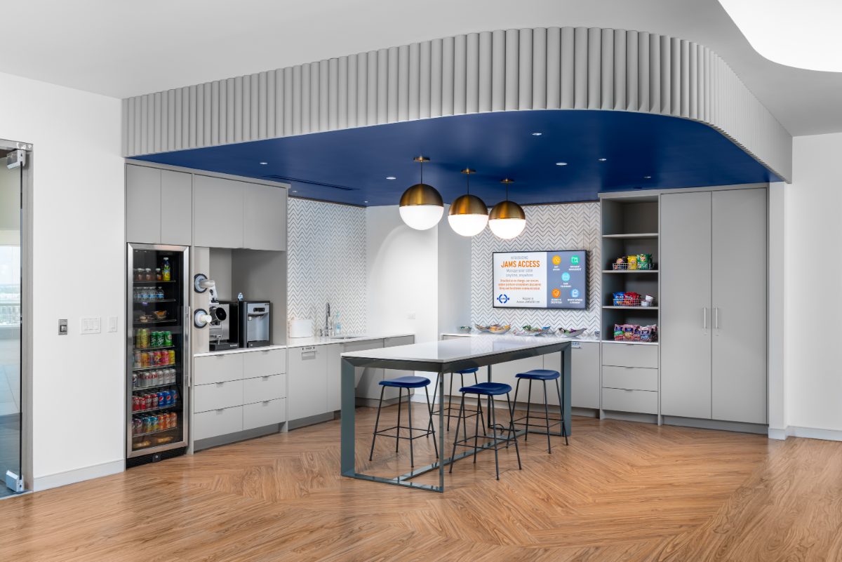 JAMS Las Vegas Café — curved cobalt soffit with fluted baffle, brass globe pendants, grey cabinetry, beverage cooler, snack pantry, herringbone wood floor.