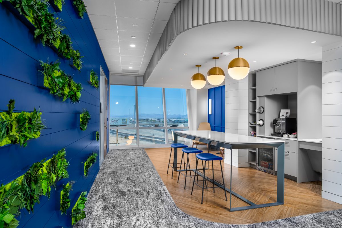 JAMS LV mini café lounge — cobalt living plant wall with box planters, brass globe pendants, quartz-top island with navy bar stools, valley view through windows.