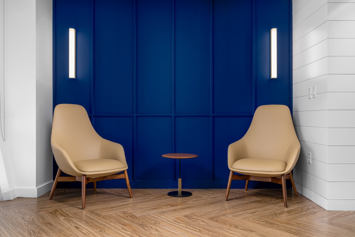 JAMS LV hallway nook — two cream leather chairs flank a walnut side table against a cobalt panel-molding wall with brass tube sconces, herringbone wood floor.