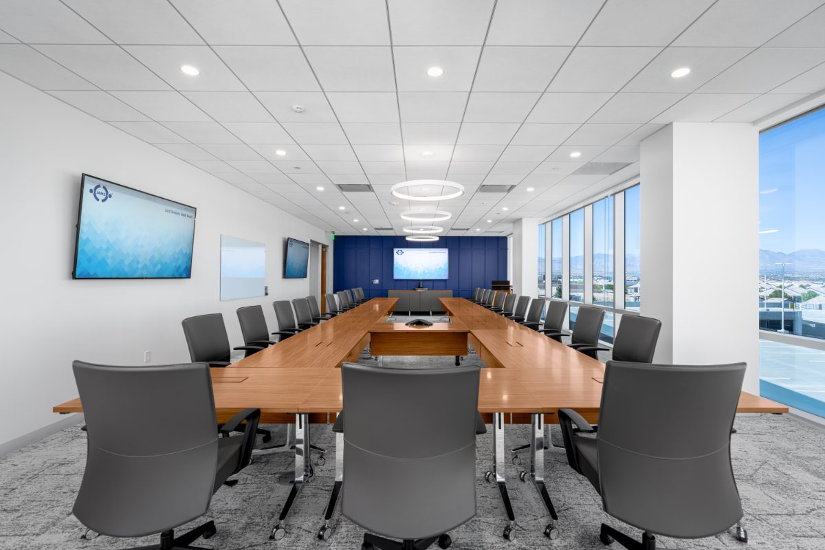JAMS LV arbitration boardroom — honey-wood U-shape table, grey leather chairs, halo ring pendants, cobalt accent wall with JAMS display, mountain view through windows.