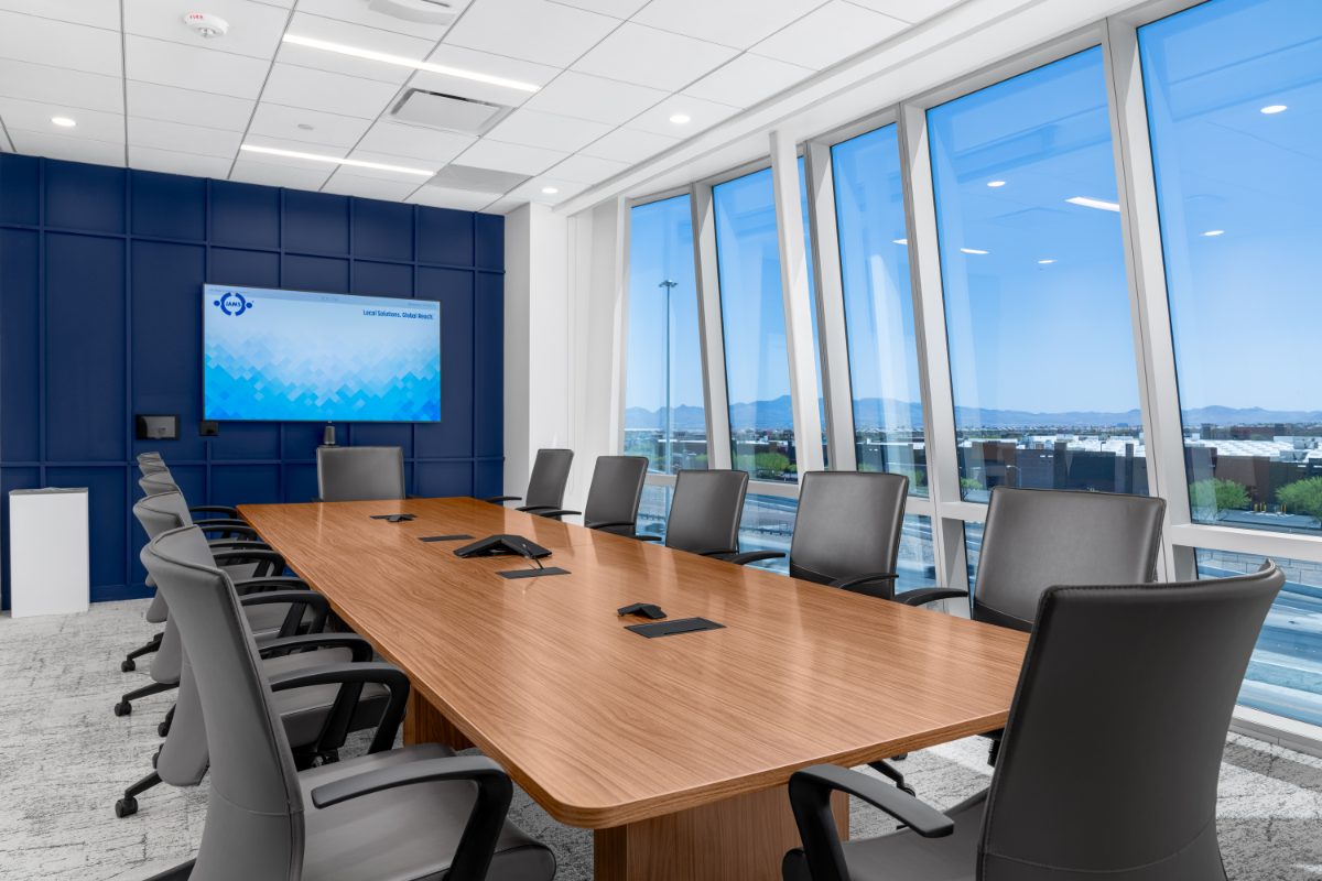 JAMS LV medium conference room — honey-wood table, grey leather chairs, cobalt panel wall with JAMS display, angled windows onto the Las Vegas valley.