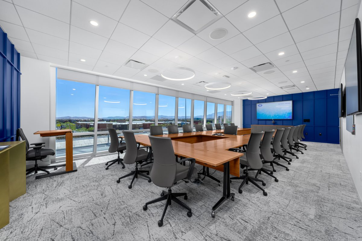 JAMS LV boardroom — honey-wood U-shape table, grey leather chairs, halo ring pendants, cobalt panel wall with JAMS display, corner windows onto valley.