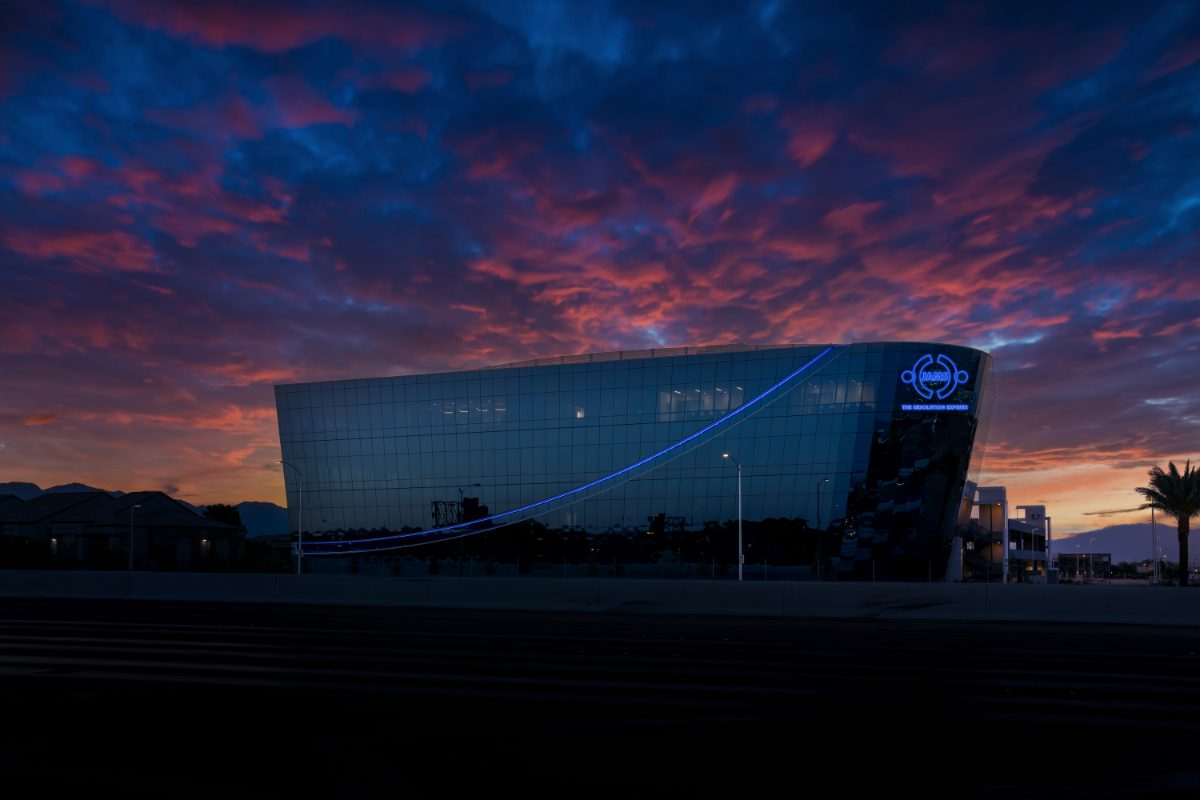 JAMS LV building at twilight — angular glass facade with curved blue LED stripe, JAMS logo lit blue against a composited purple-and-magenta cloud sky.