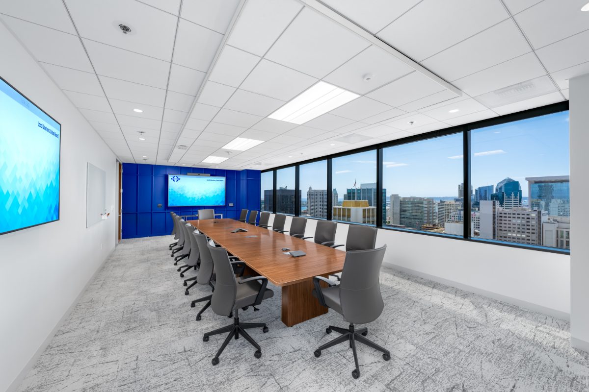 JAMS San Diego arbitration room — cherry table for fourteen with grey leather chairs, twin JAMS displays, cobalt paneled back wall, downtown skyline through windows.
