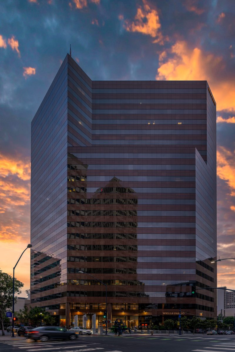 Symphony Towers at twilight — mirrored pink-bronze glass tower at 401 B Street San Diego, DLA Piper and Wells Fargo at base, motion-blurred traffic, sunset sky.