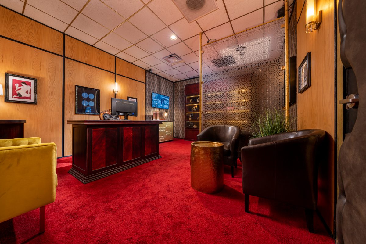 Interior of the Casino Heist escape room at PanIQ Las Vegas, styled as a 1970s casino owner's office with honey wood-paneled walls, deep red shag carpet, mahogany executive desk, y