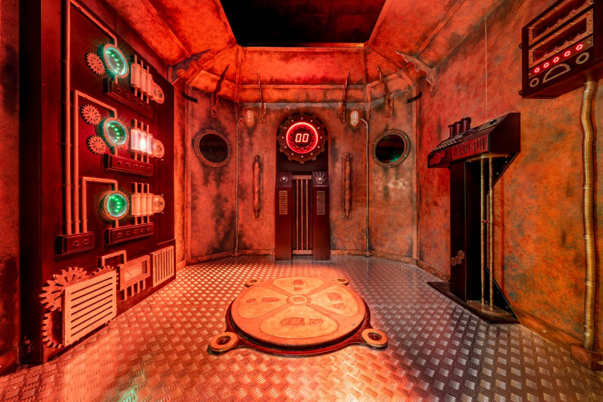 Interior of the time machine apparatus inside PanIQ Las Vegas's The Time Machine escape room — an octagonal steampunk chamber with riveted oxidized copper-and-iron walls and a diam