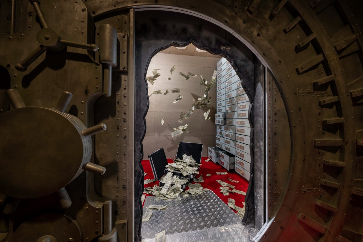 Inside view of the Casino Heist escape room vault at PanIQ Las Vegas — a heavy bronze riveted vault door cracked open with locking bolts extended, revealing a chamber with diamond-