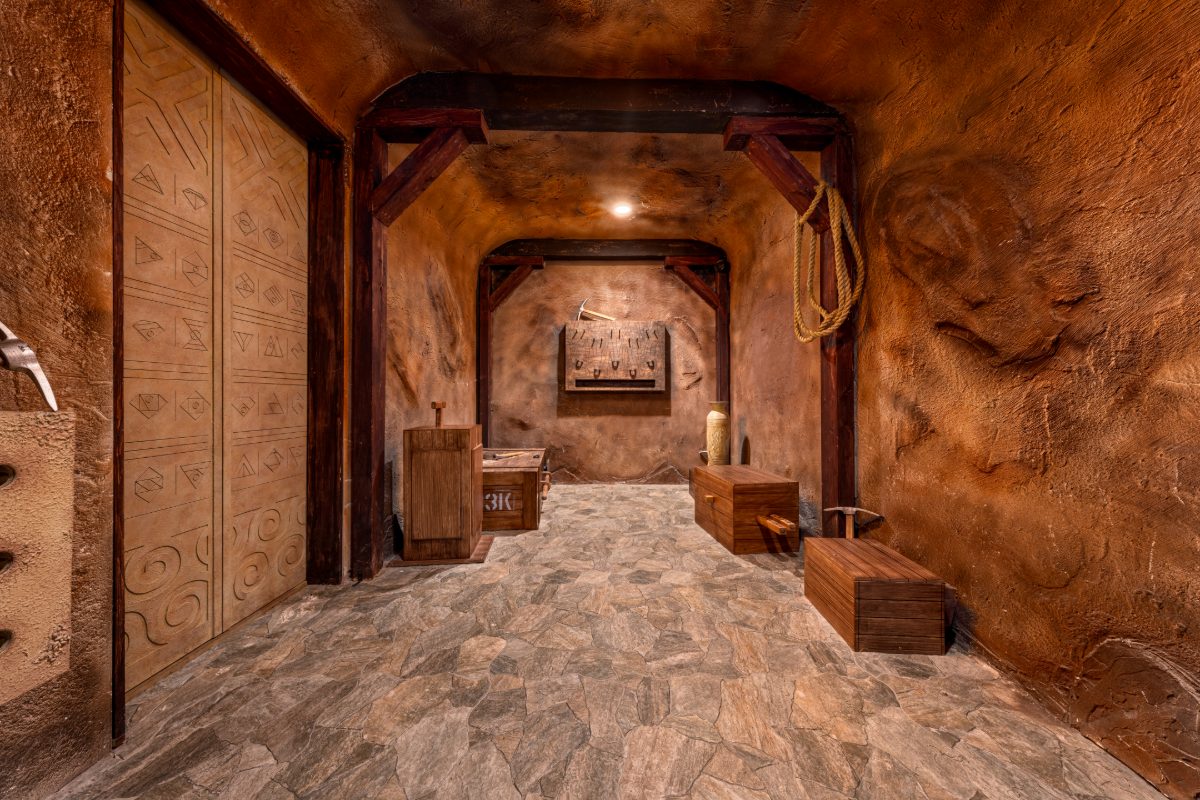The entry passage of the Atlantis Rising escape room at PanIQ Las Vegas — sculpted terracotta-toned faux-rock walls with carved Atlantean glyphs on the left and a faint relief face