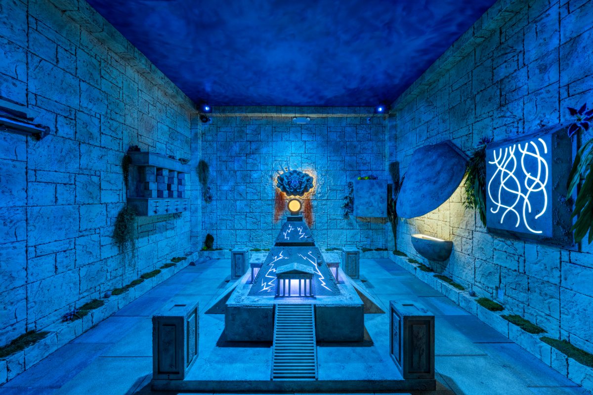 The main chamber of the Atlantis Rising escape room at PanIQ Las Vegas — a symmetrical sunken temple lit entirely in deep aquatic blue, with stacked sandstone-block walls, a steppe