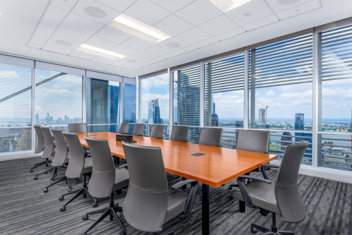 JAMS NY Conf Room 32 — long cherry table, grey leather chairs, two walls of floor-to-ceiling windows with NYT louvers framing 30 Hudson Yards, Hudson River, Jersey City.
